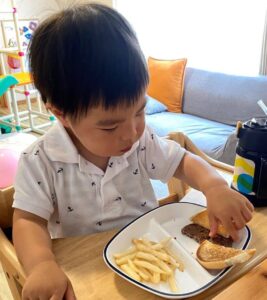 子どもがハンバーガーを手に取る、お皿の上にポテトとハンバーガーが置いてある写真
